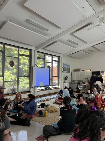 group of people sitting in a angular room. Light outside, and a projector is there. Focussed.