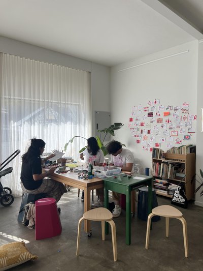 colourful postcards in a cosy room, people on stools creating